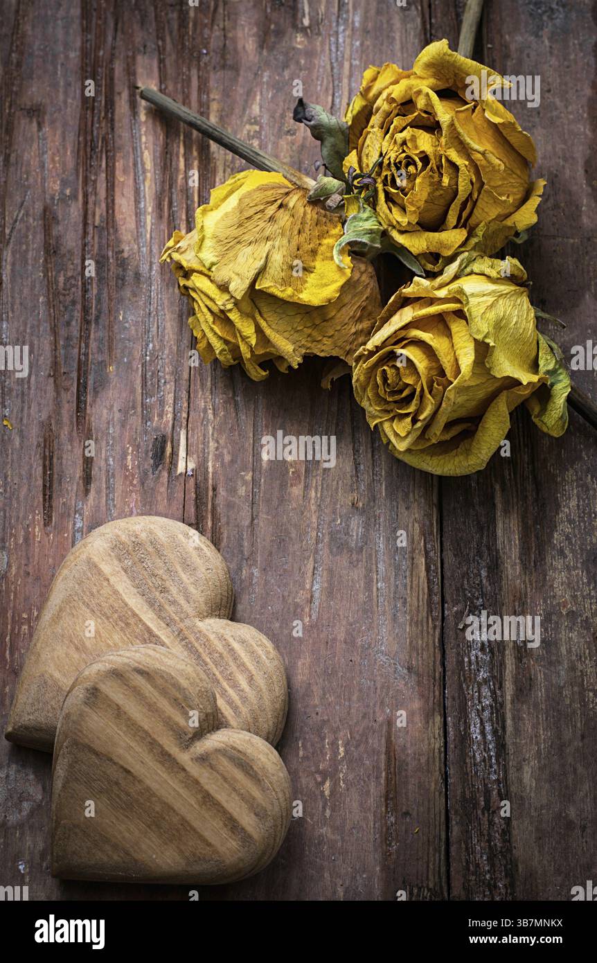 Cuore simbolico in legno intagliato a mano su uno sfondo di rose gialle Foto Stock