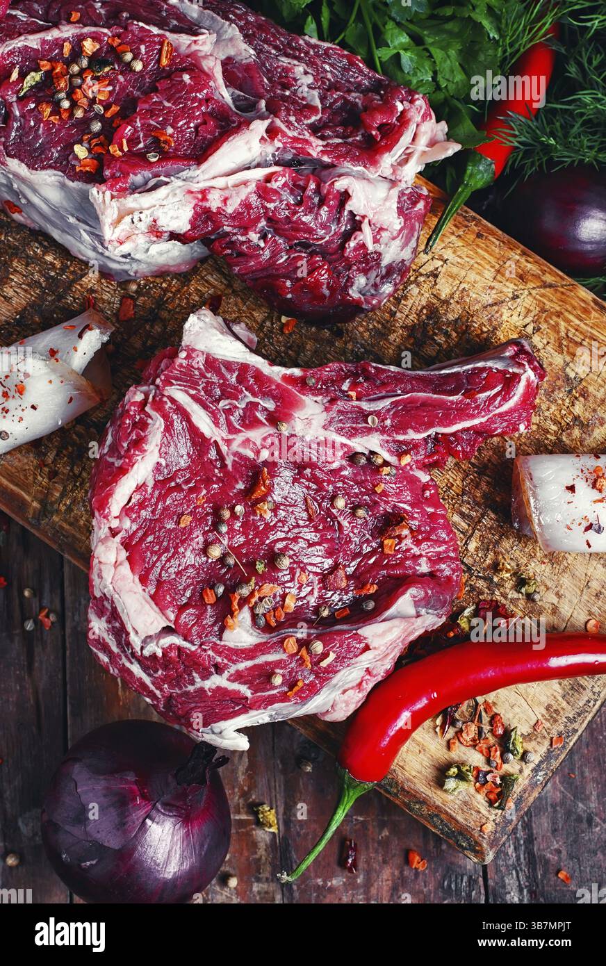 Un trito di pezzi di carne di manzo crudo con spezie sul tagliere di legno Foto Stock