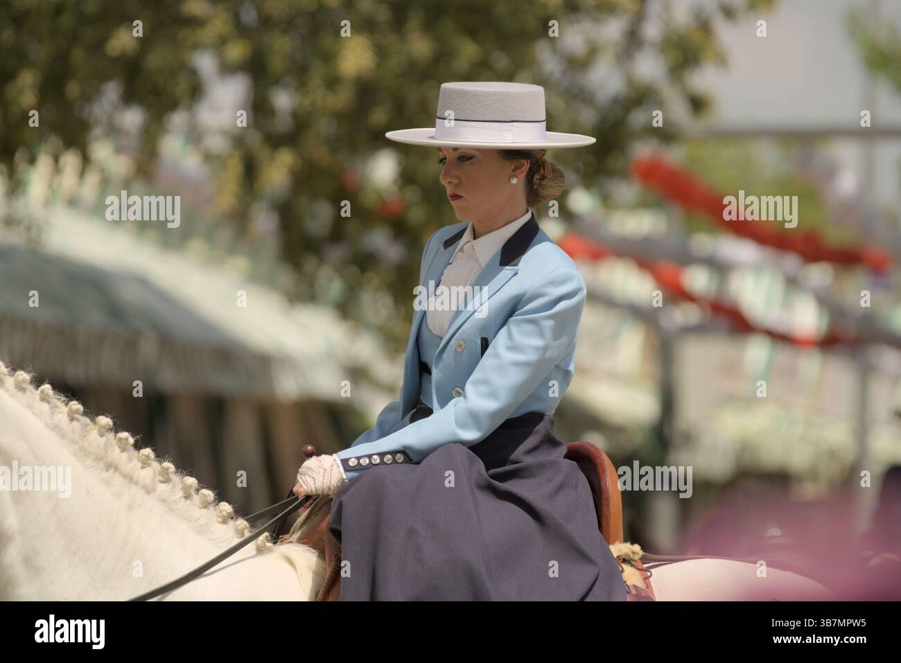 Elegante donna andalusa in traje corto azzurro che attraversa la Feria de Sevilla 2025, incarnando la grazia equestre e la tradizione spagnola. Foto Stock