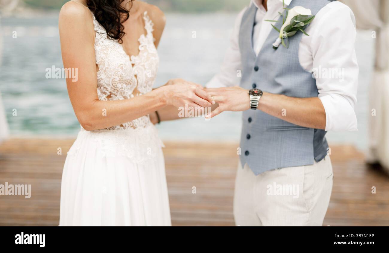 La sposa mette l'anello nuziale sul dito dello sposo durante la cerimonia nuziale sul mare . Foto Stock