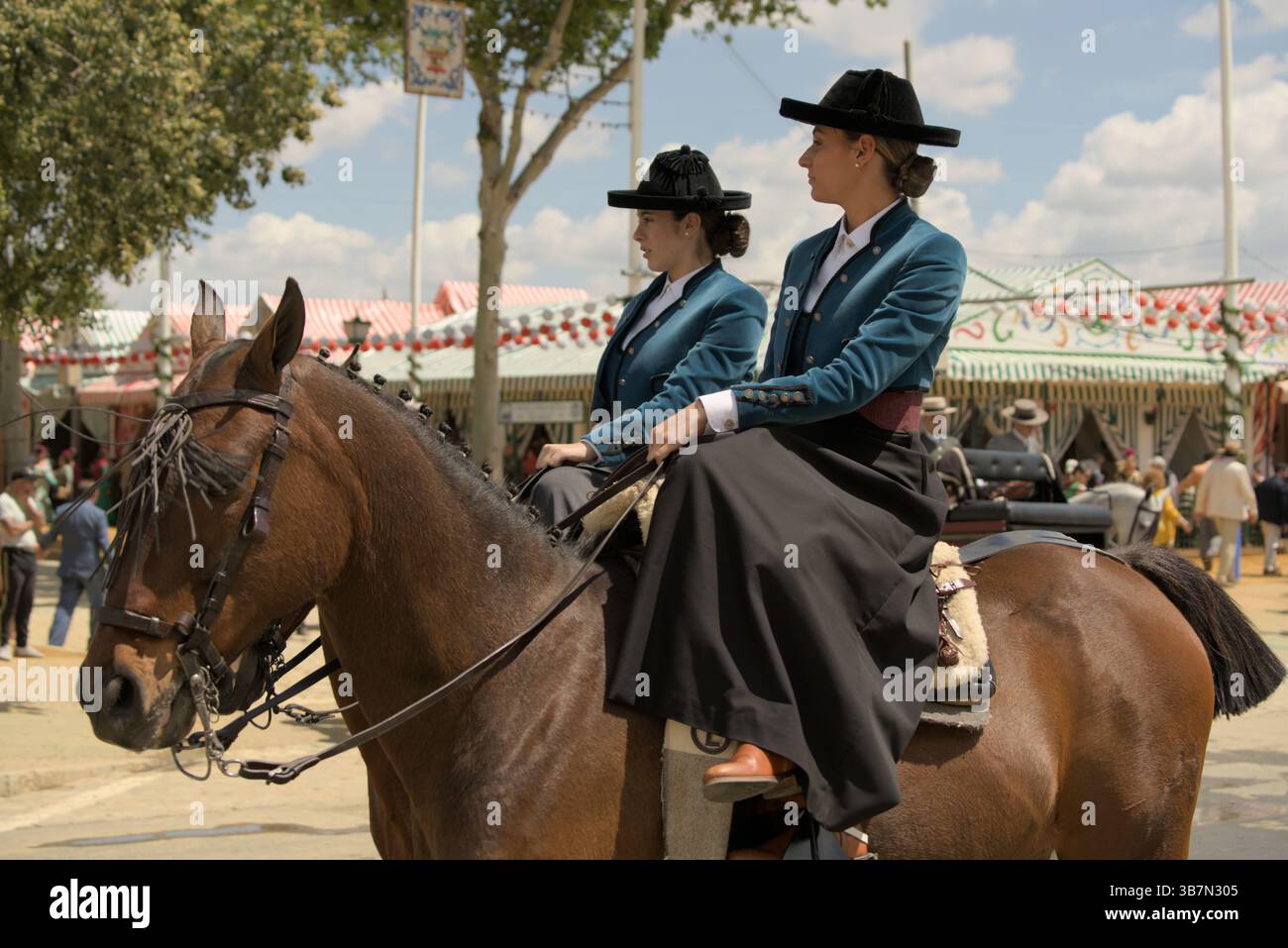 Donne andaluse nel tradizionale traje corto che cavalcano attraverso la Feria de Sevilla 2025, celebrando l'eleganza e il patrimonio equestre. Feria de Sevilla Foto Stock