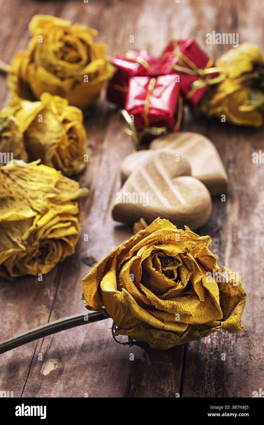 Cuore simbolico in legno intagliato a mano su uno sfondo di rose gialle Foto Stock