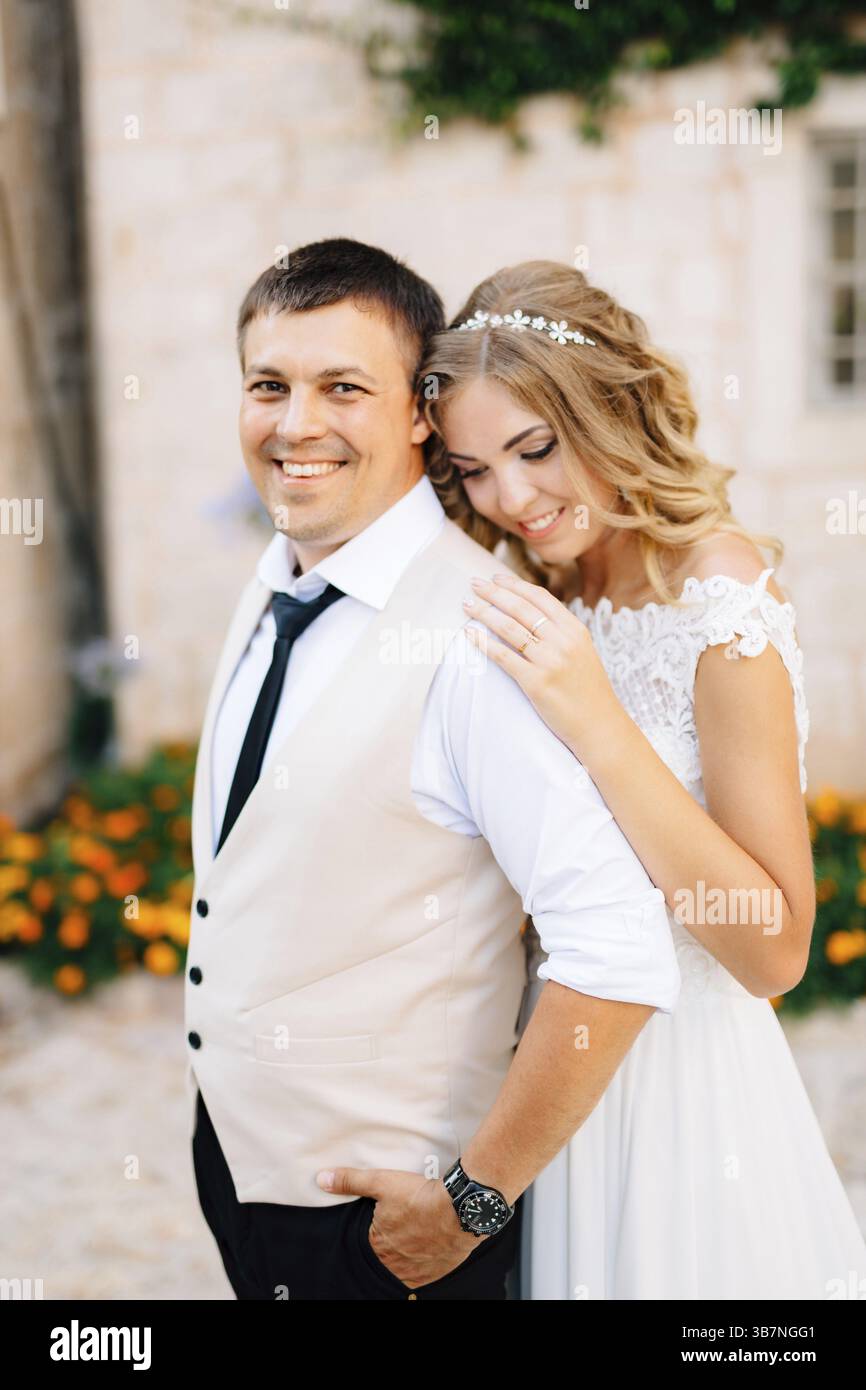 La sposa sta abbracciando lo sposo per le strade di Perast vicino a case di mattoni bianchi. Foto Stock