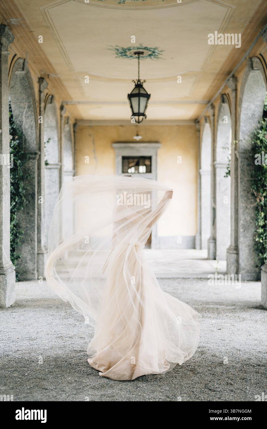 La sposa con un abito da sposa si stende ricoperta di un velo su una vecchia terrazza a pilastri. Lago di Como. Foto Stock