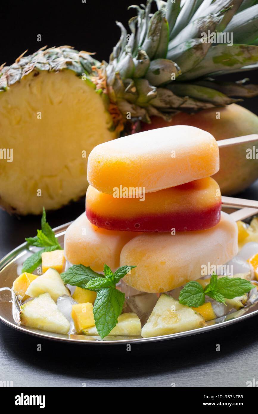 Il gelato all'ananas di mango impilato su un piatto d'argento è guarnito con foglie di menta e accompagnato da frutta appena tagliata. Gli ananas tropicali aggiungono un'atmosfera vivace. Foto Stock