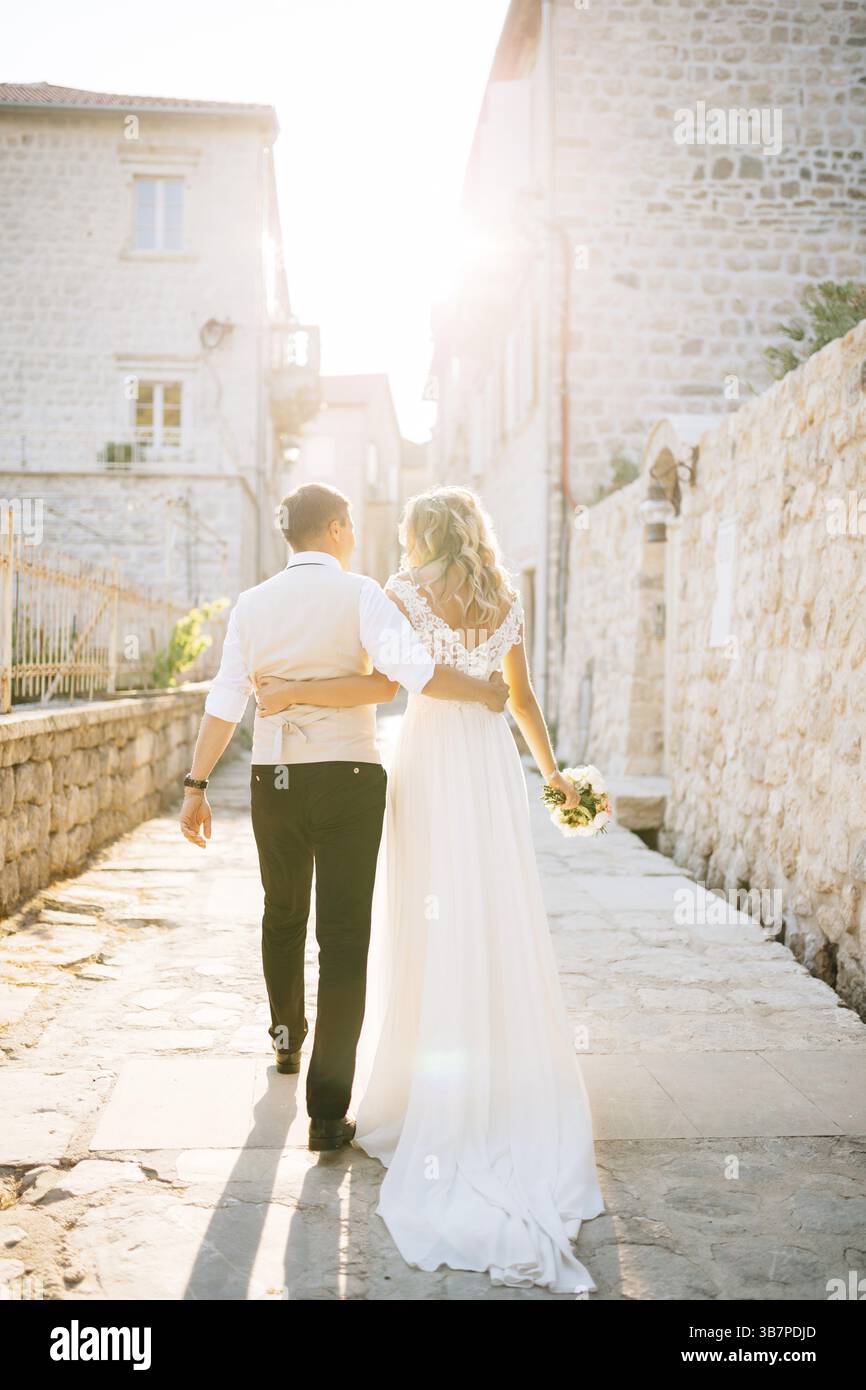 La sposa e lo sposo si abbracciano lungo le strade di Perast, accanto alle case in mattoni bianchi, vista sul retro. Foto Stock