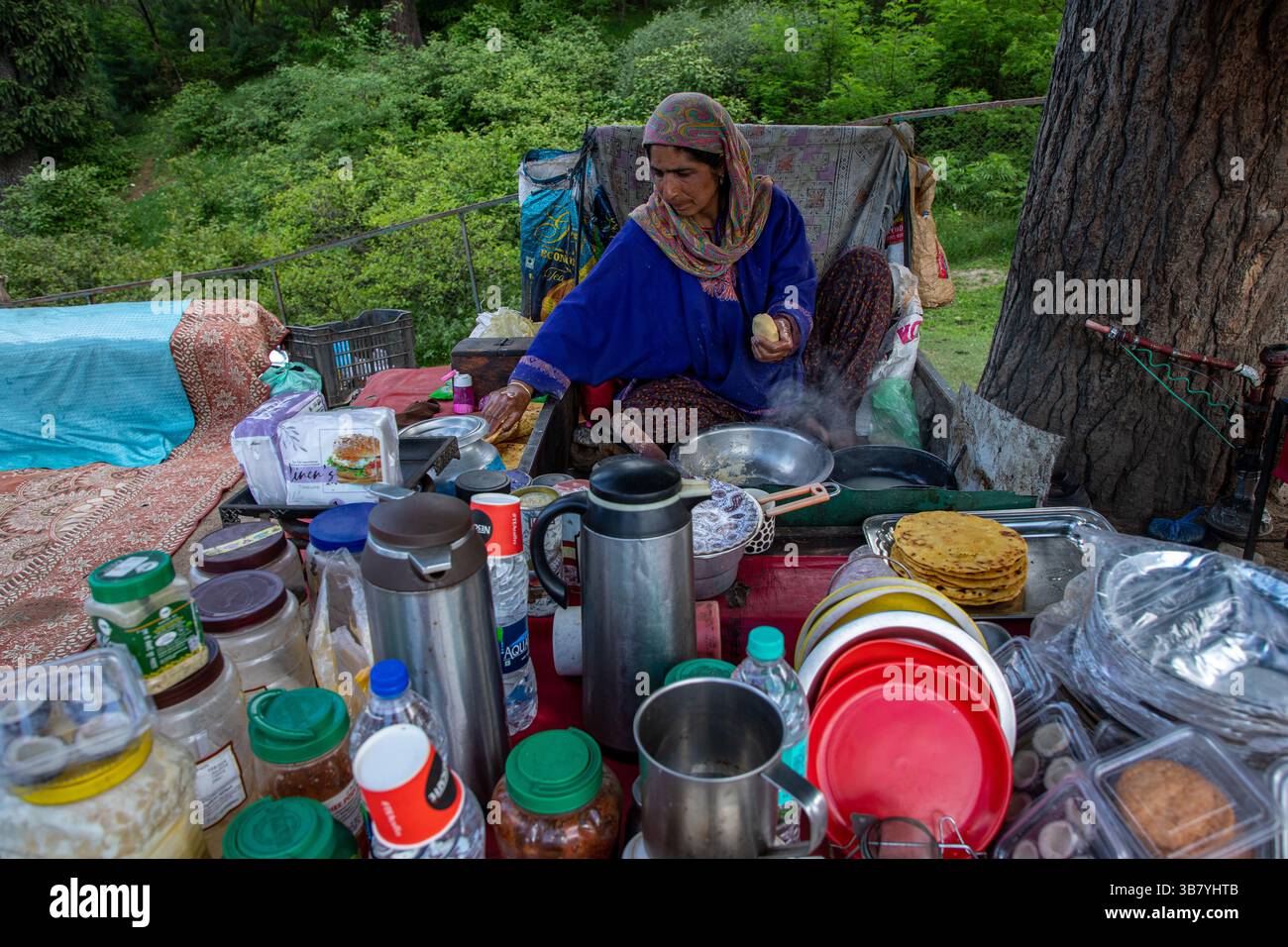 23 maggio 2024, Doodhpathri, Jammu e Kashmir, India: Una donna del Kashmir prepara tortillas di farina di mais mentre vende Noon Chai (tè salato) ai turisti e alla gente del posto passando per la sua banchina lungo la strada Doodhpathri nel distretto di Budgam, a sud-ovest di Srinagar. Le autorità hanno chiesto ai proprietari dei venditori di tè di liberare lo spazio che hanno occupato ''illegalmente'' entro dieci giorni o di affrontare azioni. I funzionari hanno detto a un'agenzia di stampa locale che l'autorità per lo sviluppo del turismo ha ricevuto numerose lamentele per il fatto che i proprietari delle bancarelle di tè hanno tagliato rami di alberi, danneggiando così le immagini Foto Stock