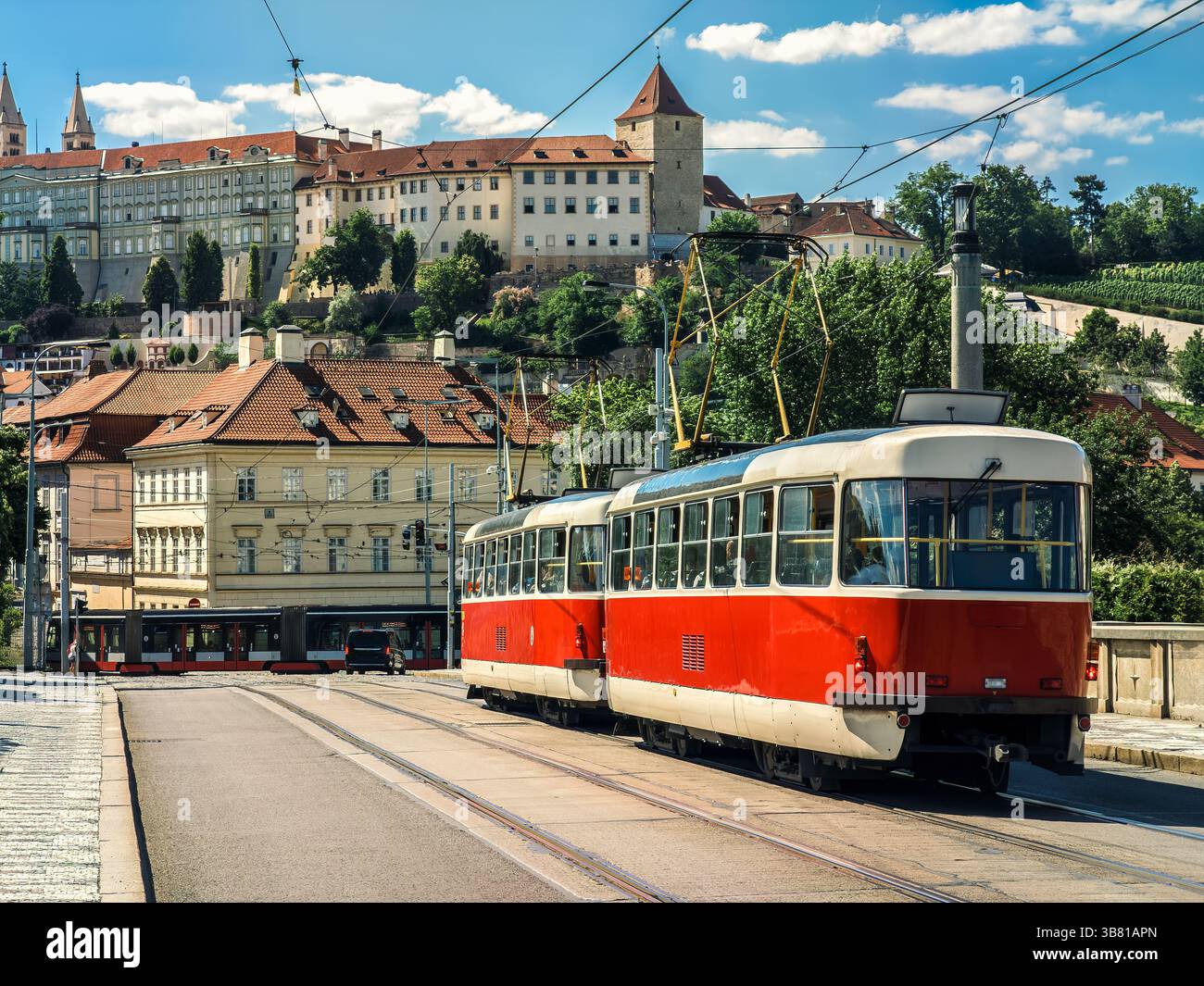 Un vivace tram rosso e bianco viaggia lungo i suoi binari sul ponte, sullo sfondo di edifici storici a Praga, Repubblica Ceca. Foto Stock