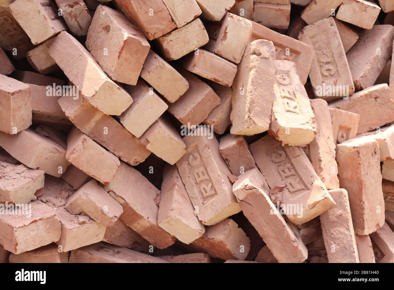 L'immagine mostra una pila di mattoni marrone-rossastro, ciascuno timbrato con lettere, sullo sfondo della luce naturale del sole. Le diverse trame di superficie vengono aggiunte Foto Stock