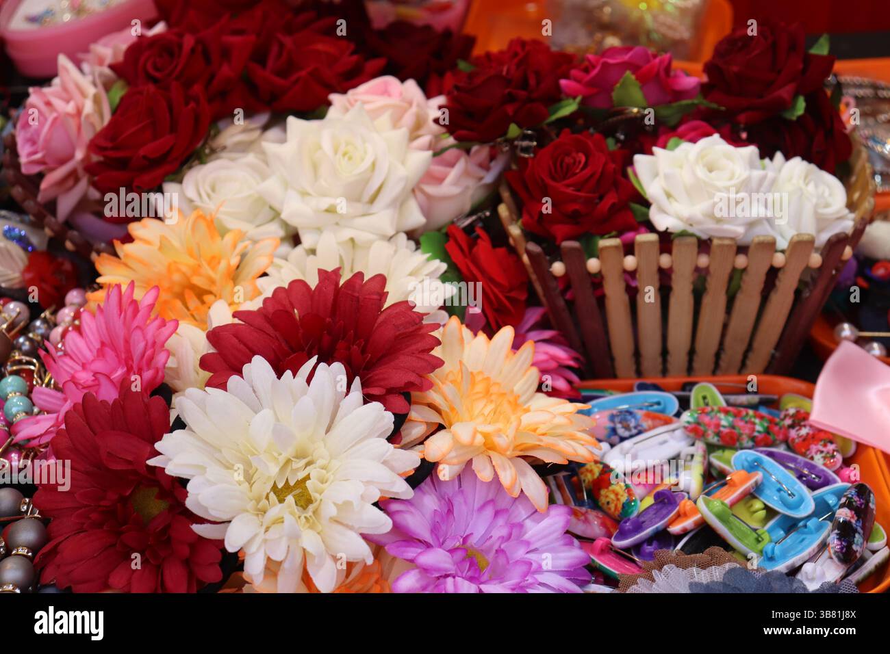 Le vivaci rose e le margherite nelle tonalità rosso, rosa e bianco creano un assortimento sorprendente, accuratamente sistemato con clip per capelli e un cesto in legno per un beaut Foto Stock