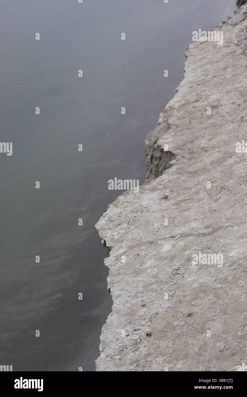 La nitida vista aerea mostra il netto contrasto tra una scogliera bianca frastagliata, elevata e rocciosa e l'acqua cupa, ferma e torbida che si affaccia su di essa Foto Stock