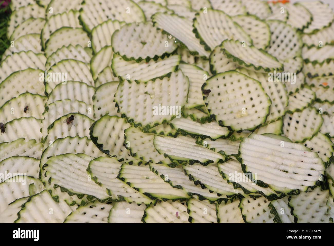 Questo primo piano presenta numerosi pezzi di zucchine tagliate a fette di waffle disposti a fondo, creando motivi di consistenza e colore. Possono essere presenti diverse piccole mosche Foto Stock