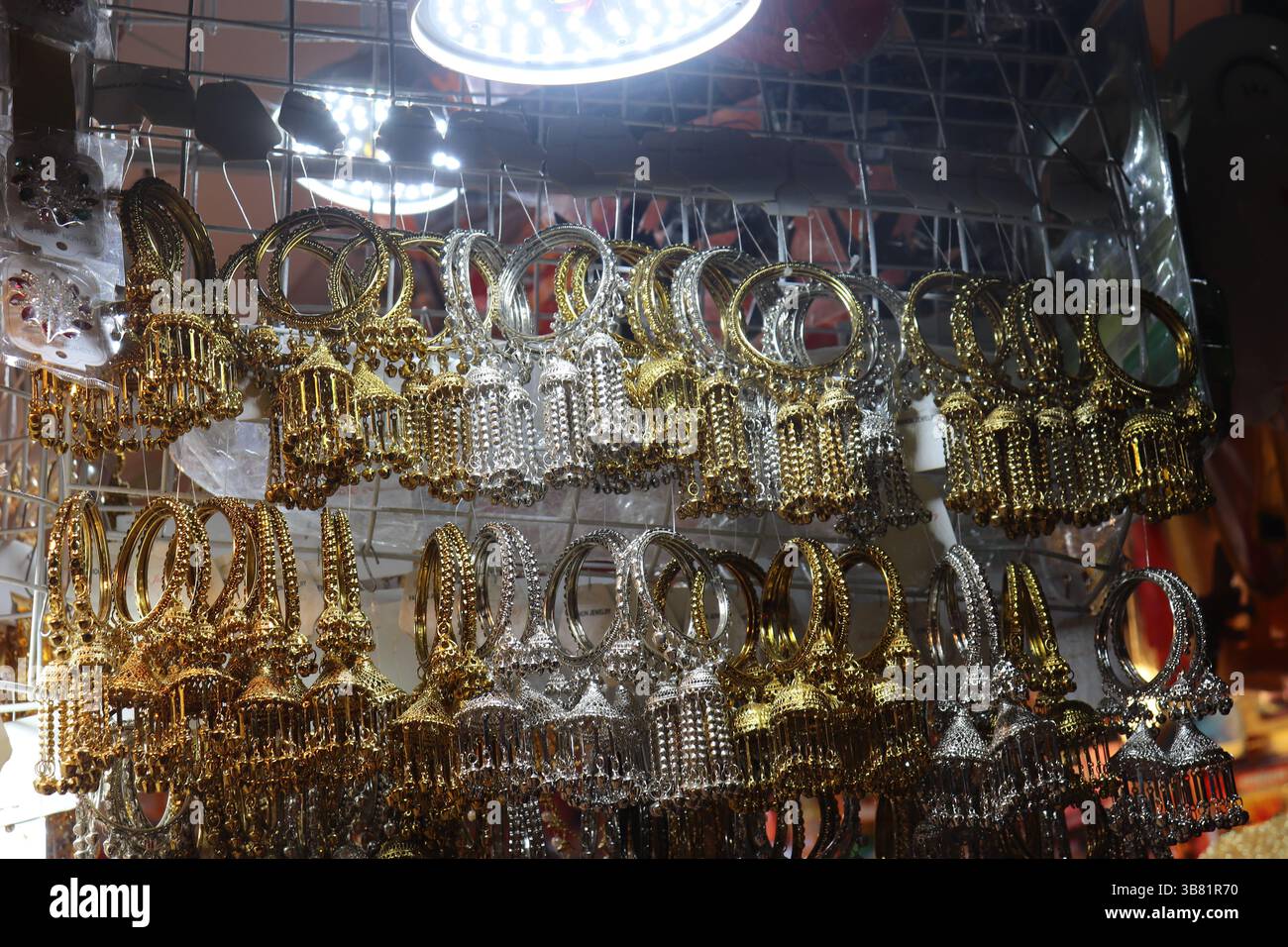 Un'incredibile gamma di bracciali rigidi tradizionali in oro e argento con perline penzolanti sono esposti in vendita, illuminati da un'illuminazione luminosa a soffitto all'interno di un Foto Stock