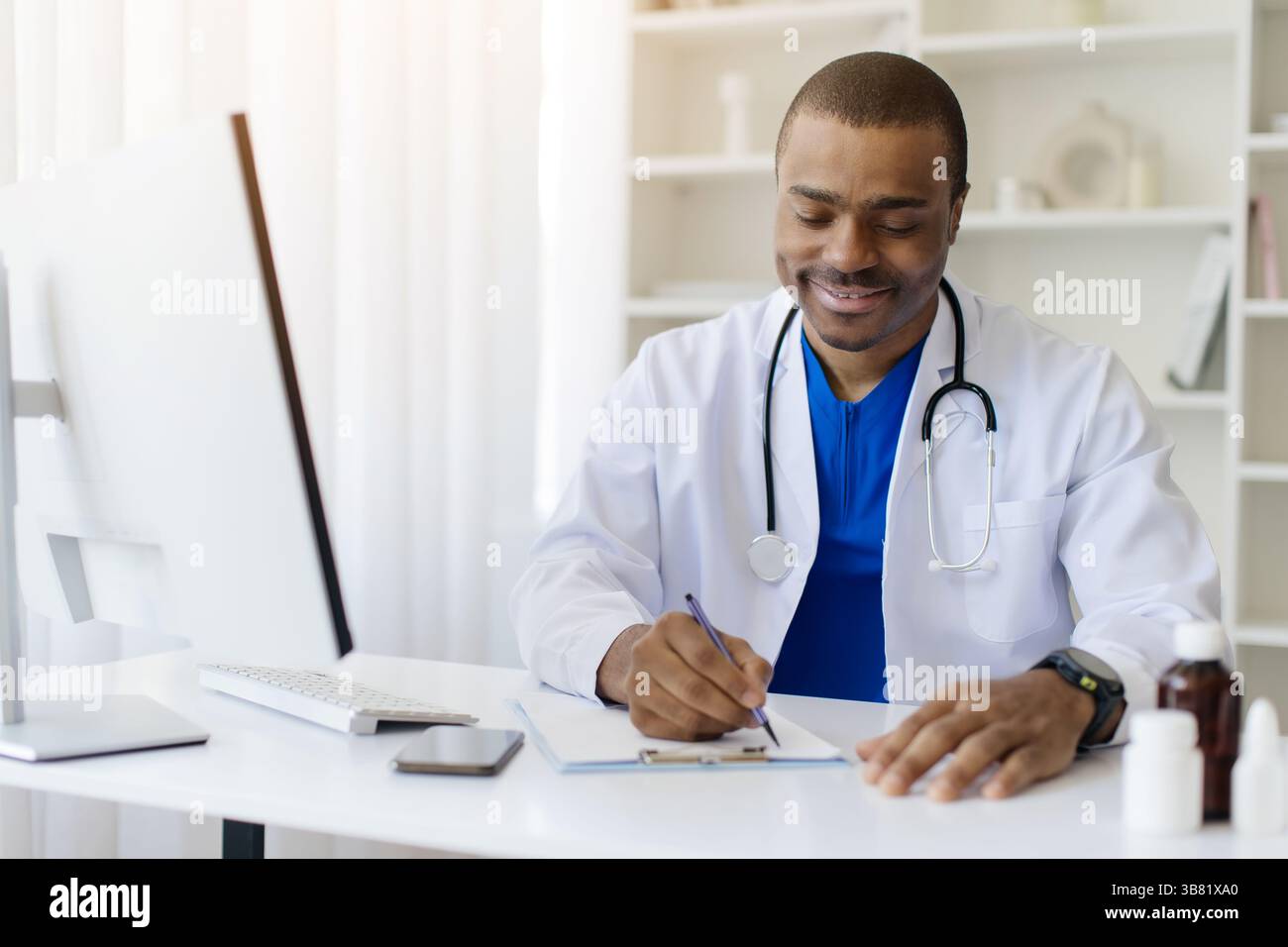 Medico afroamericano che scrive sugli appunti seduto alla scrivania in ufficio Foto Stock