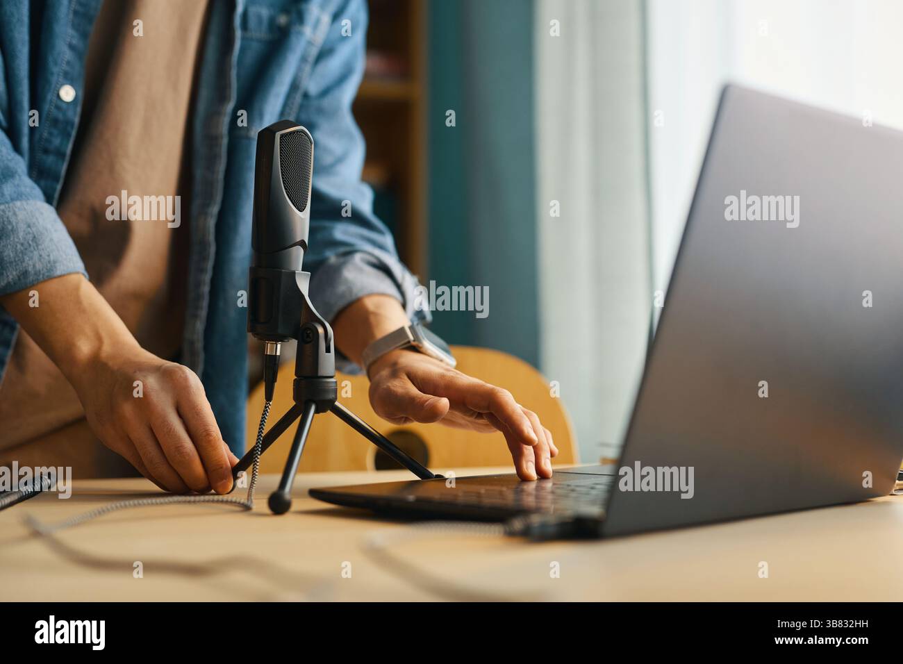 Microfono regolabile e utilizzo di un computer portatile in ufficio con abbigliamento casual per creare contenuti o svolgere attività di lavoro. Finestra sullo sfondo Foto Stock