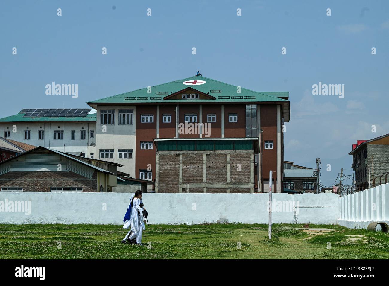 Srinagar, India. 7 maggio 2025. Le ragazze della scuola kashmiri passano davanti a un lavoratore che dipinge un simbolo a croce rossa sul tetto di un ospedale come misura preventiva in mezzo alle tensioni di confine in corso. India e Pakistan si scambiarono artiglieria pesante lungo la loro frontiera contesa il 7 maggio dopo che nuova Delhi lanciò attacchi missilistici mortali sul suo arcinemico, nella peggiore violenza tra i vicini armati di armi nucleari degli ultimi due decenni. (Foto di Faisal Bashir/SOPA Images/Sipa USA) credito: SIPA USA/Alamy Live News Foto Stock