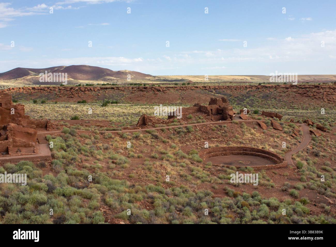 Le rovine di un'antica civiltà sono sparse in un paesaggio desertico asciutto, con strutture in pietra visibili tra arbusti e montagne lontane sotto a. Foto Stock