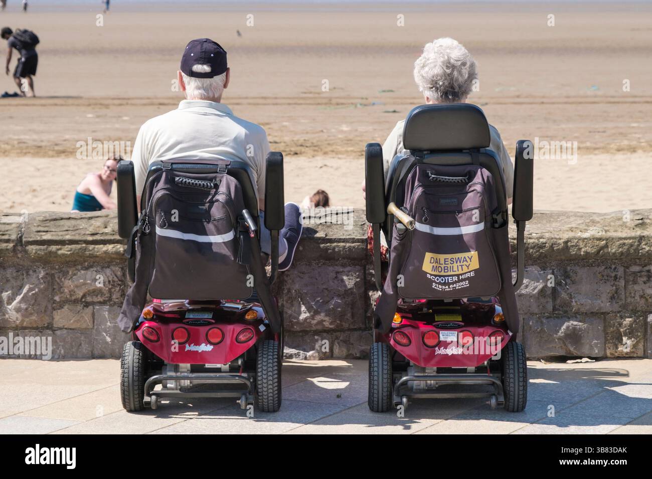 due persone su scooter mobili sedevano sul lungomare di weston-super-nare godendosi il mare Foto Stock