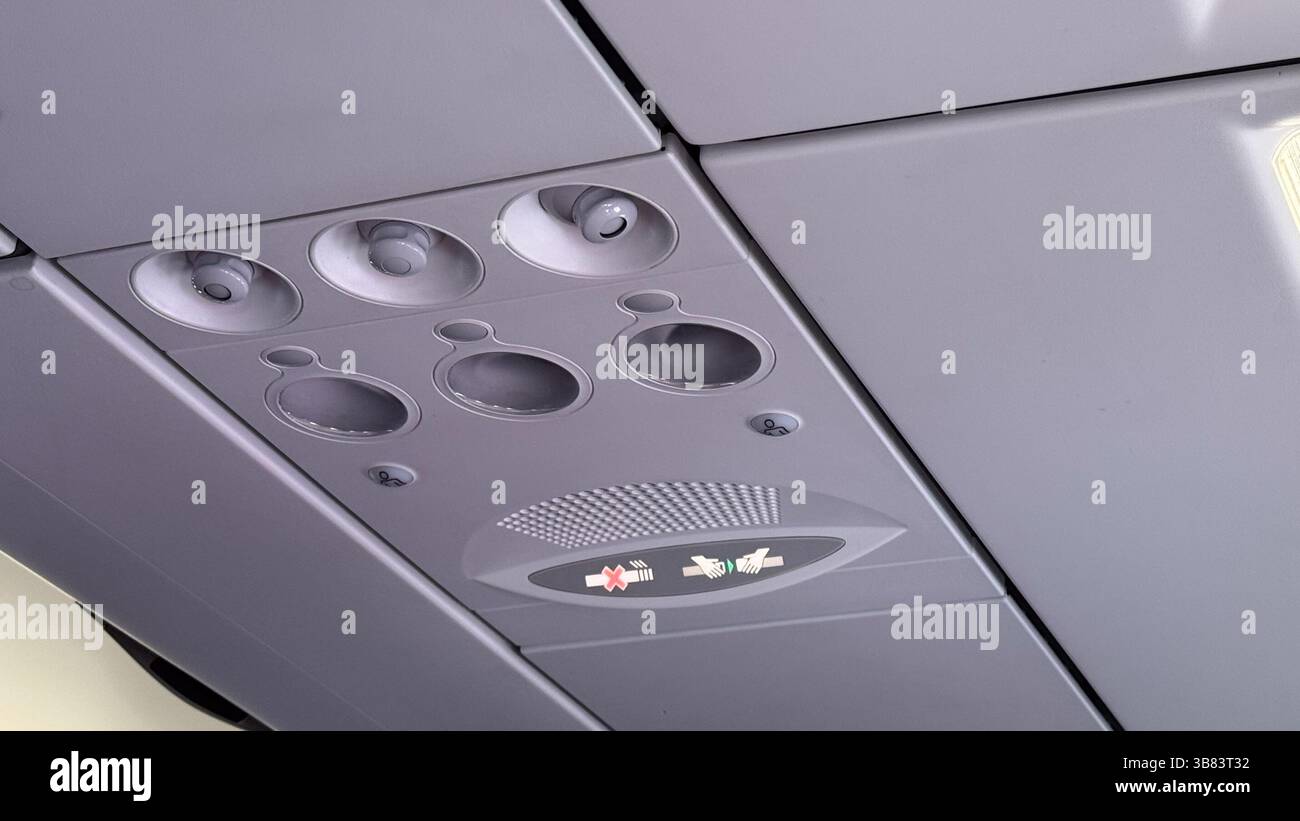 Pannello di controllo aereo a soffitto con prese d'aria circolari, cintura di sicurezza illuminata e segnali di divieto di fumo. Foto Stock
