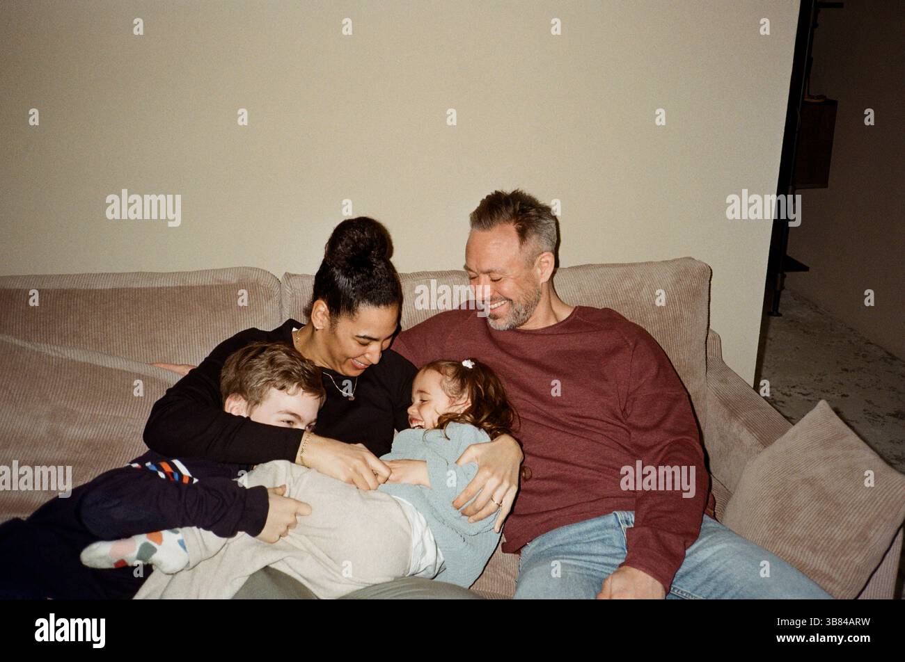 Padre e madre trascorrono il tempo libero con i bambini seduti sul divano di casa Foto Stock
