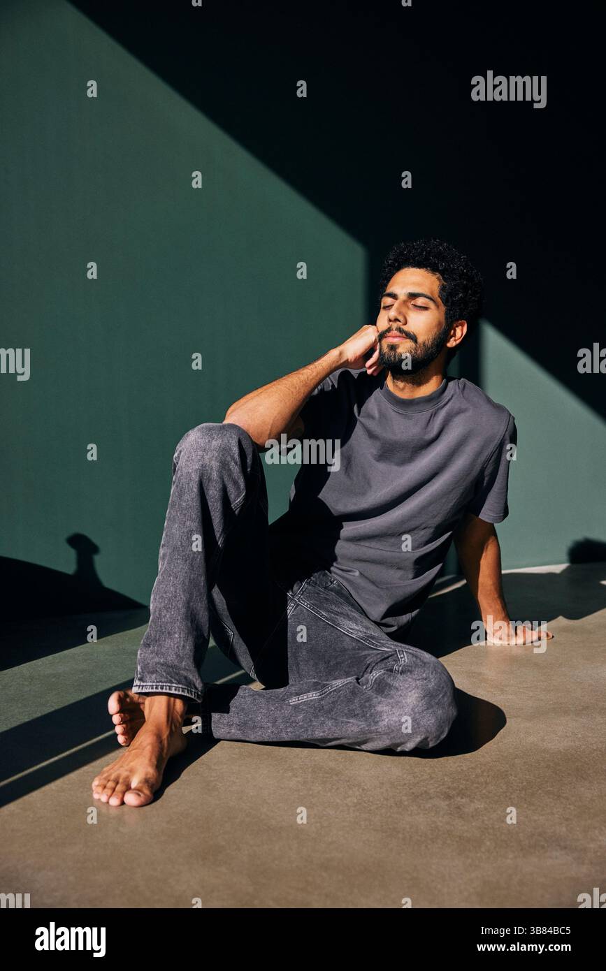 Uomo appoggiato al gomito con gli occhi chiusi seduto sul pavimento di casa Foto Stock