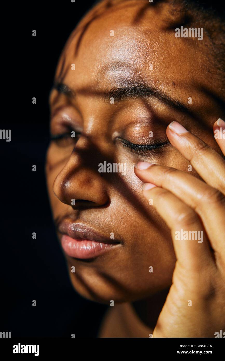 Primo piano della luce del sole che splende sulla donna con gli occhi chiusi tenendo la mano sul viso Foto Stock
