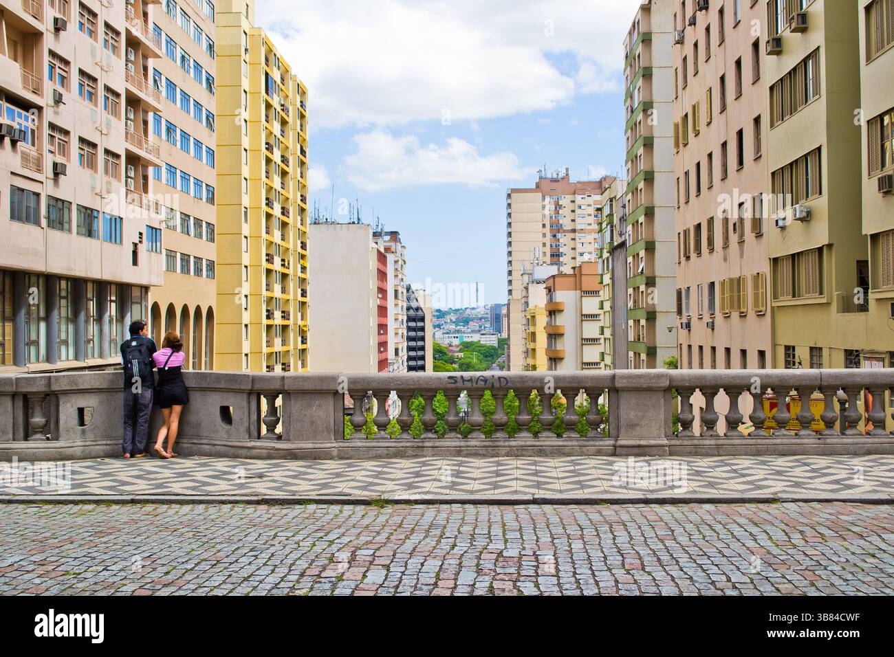 coppia sulla guardia del corpo di un vecchio ponte che contempla la vista della città in un giorno di cielo blu con nuvole bianche. Foto Stock