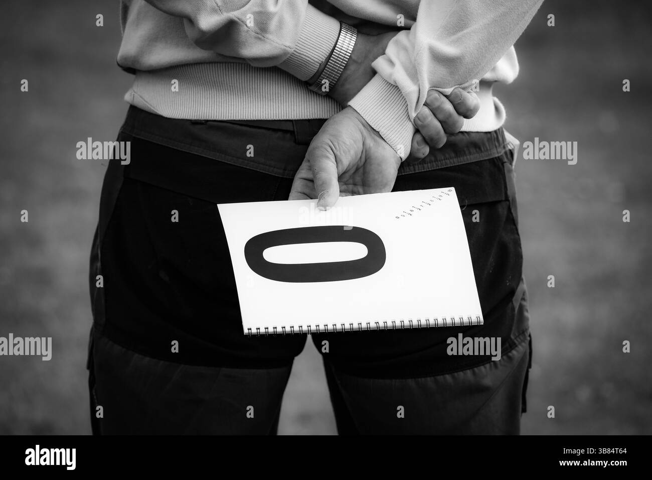 Un giudice detiene un tabellone di valutazione con un punteggio zero alle sue spalle mentre i partecipanti alla competizione agilità attendono il loro turno per mostrare le abilità in un'area erbosa. Foto Stock