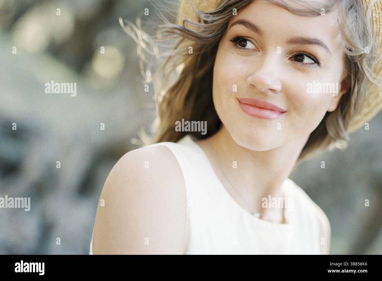 Donna sorridente in un cappello di paglia con i capelli che soffiano nel vento. Verticale. Foto Stock