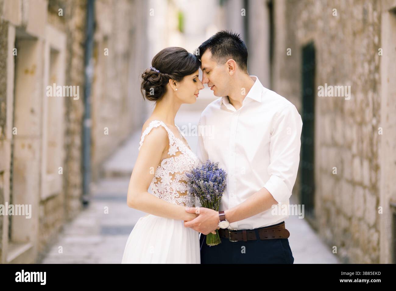 Sibenik, Croazia - 05.06.17: Lo sposo appoggiò la fronte alla fronte della sposa con un bouquet di lavanda in un abito bianco sullo sfondo di Foto Stock