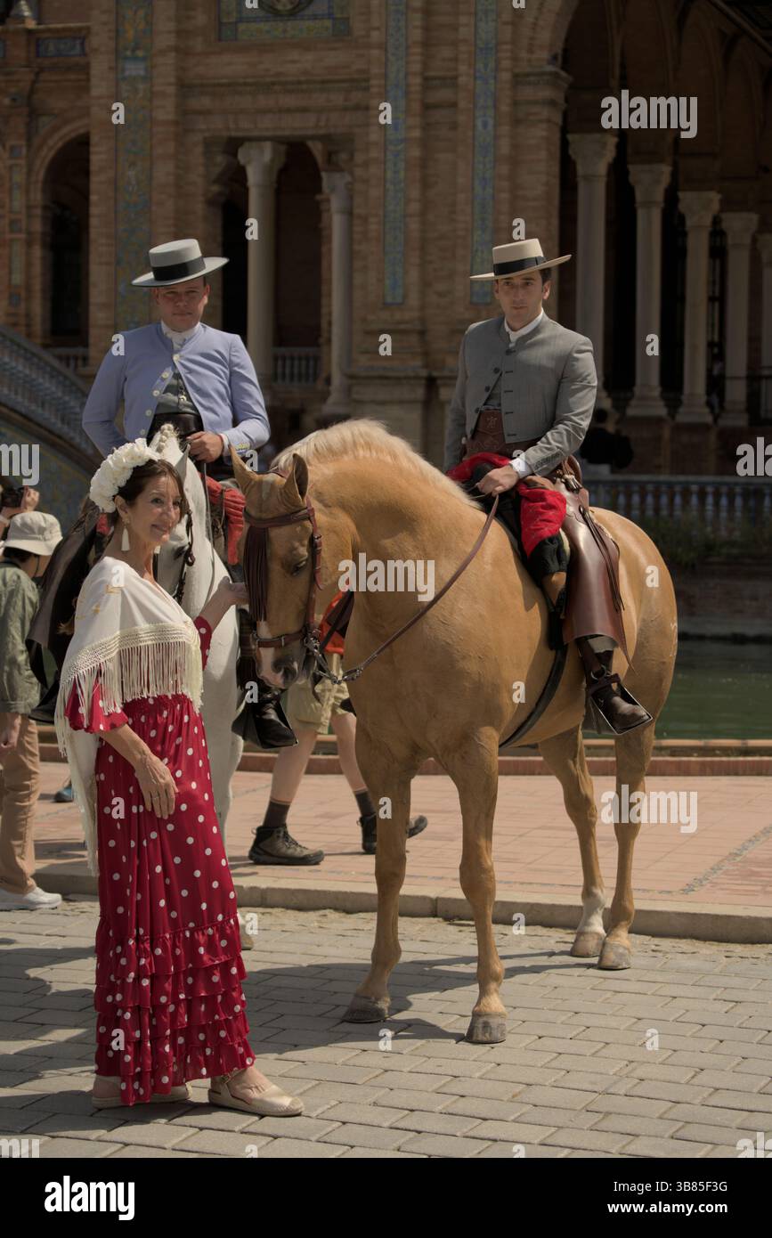 Cavalieri andalusi e una donna in un abito rosso flamenco a Plaza de España durante la Feria de Sevilla 2025, Siviglia, Andalucía, Spagna. Foto Stock