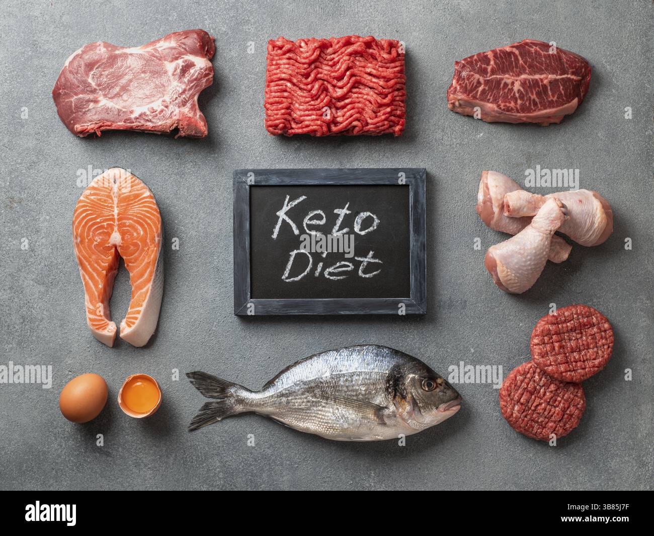 Dieta cheto concetto. Materie prime per la dieta povera di carboidrati - carne, pollame, pesce, frutti di mare, uova, carni bovine le ossa per il brodo di osso e parole cheto dieta su pietra grigia Foto Stock