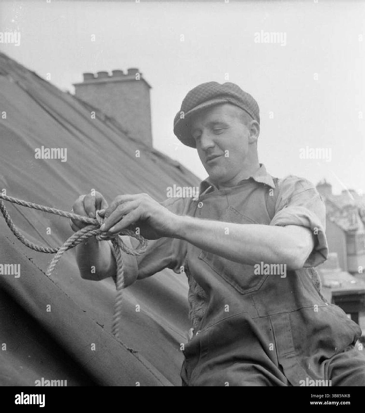Il costruttore J Naitby (di Darlington) collega la tela cerata al tetto di una casa danneggiata da una bomba volante V1. Il signor Naitby fa parte della "Blitz Repair Squad", un team di costruttori che sono venuti a Londra da varie parti del paese per riparare tali danni. Foto Stock
