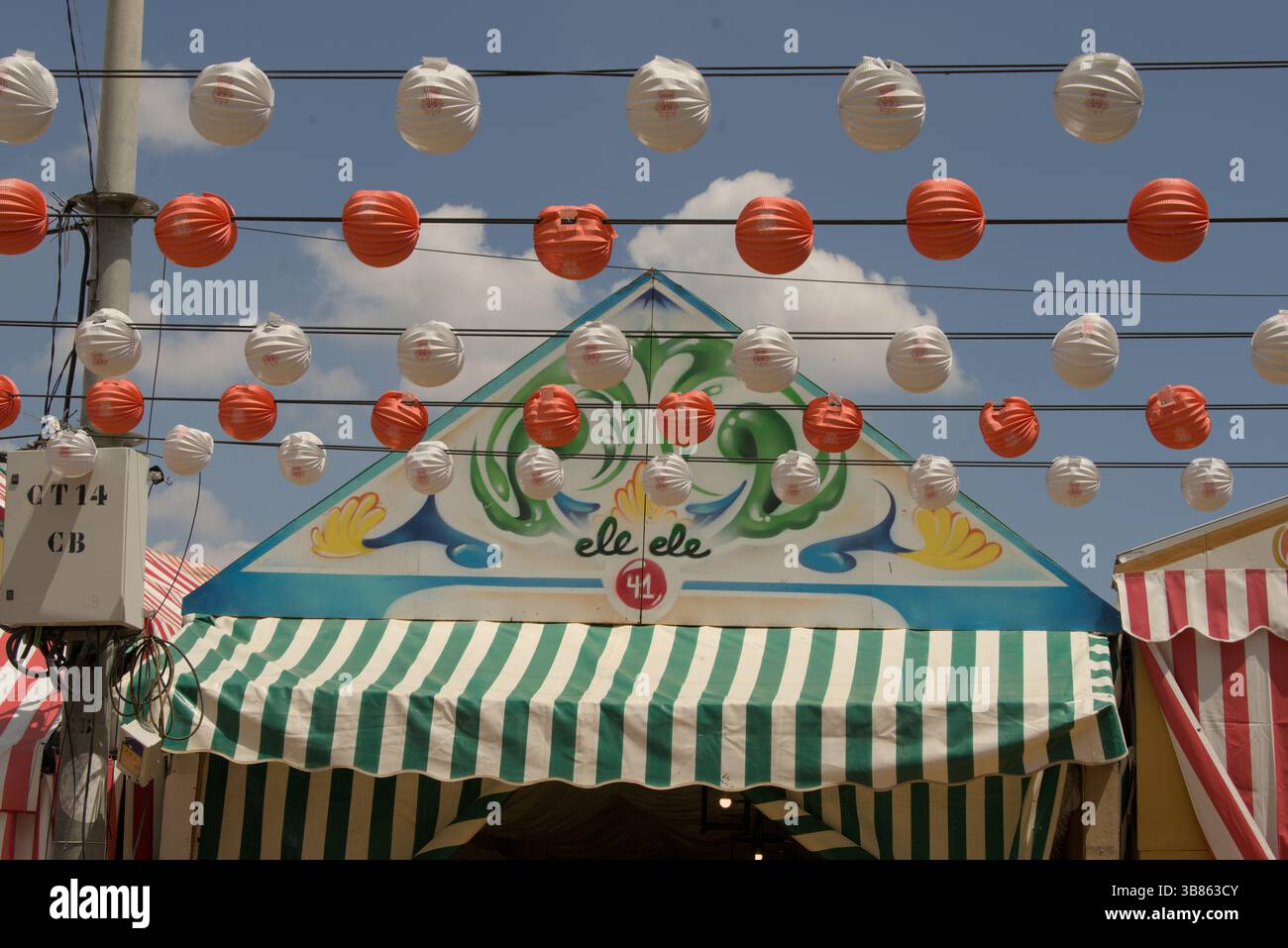 Tenda Feria de Abril decorata "El Ele" a Siviglia, Andalusia, Spagna, con lanterne colorate e tende da sole a righe verdi sotto un cielo soleggiato. Foto Stock