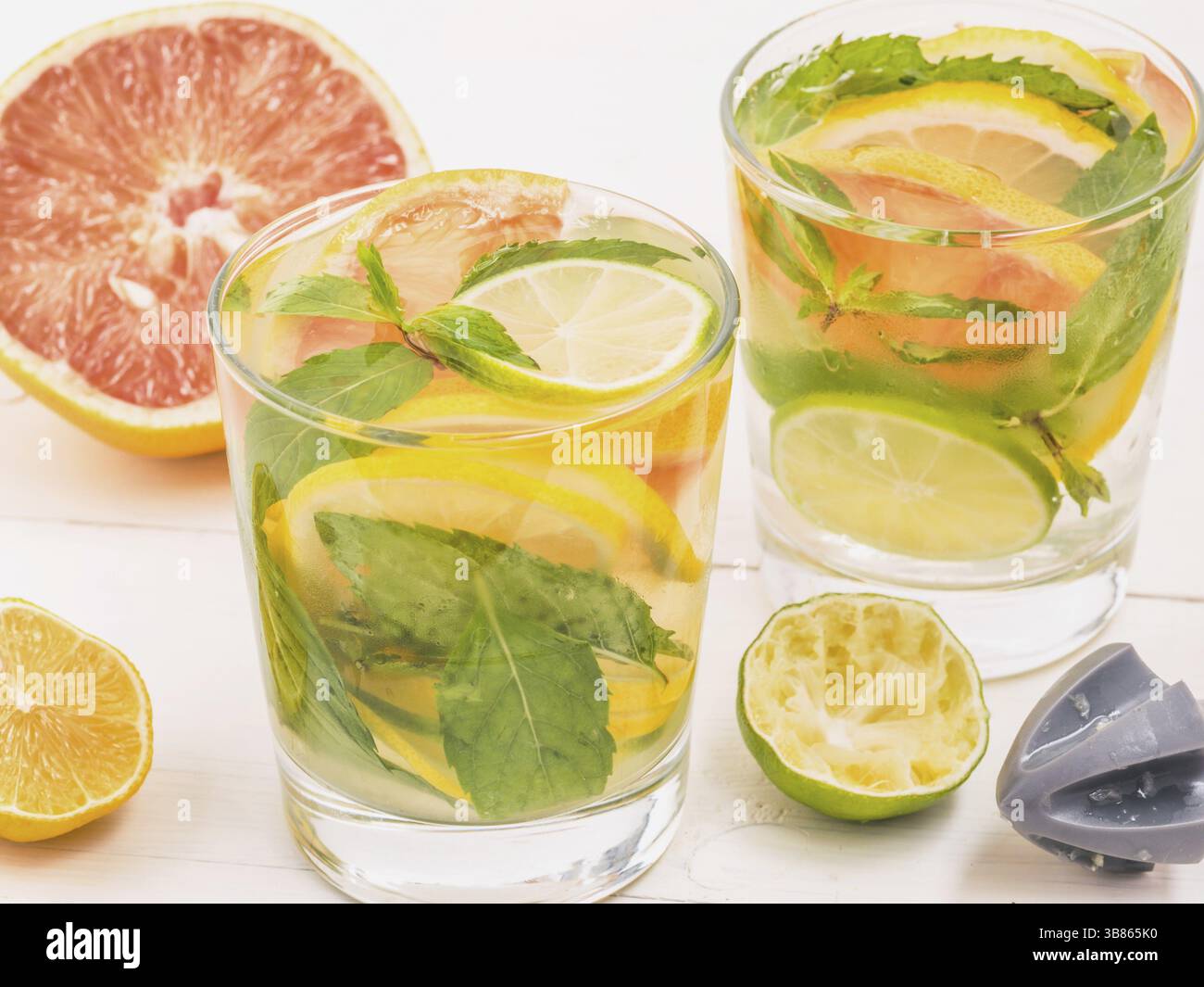 Freddo limonata fatta in casa con limone fresco, calce, pompelmo e menta da alesatore di limone. Bevanda estiva sul bianco sullo sfondo di legno Foto Stock