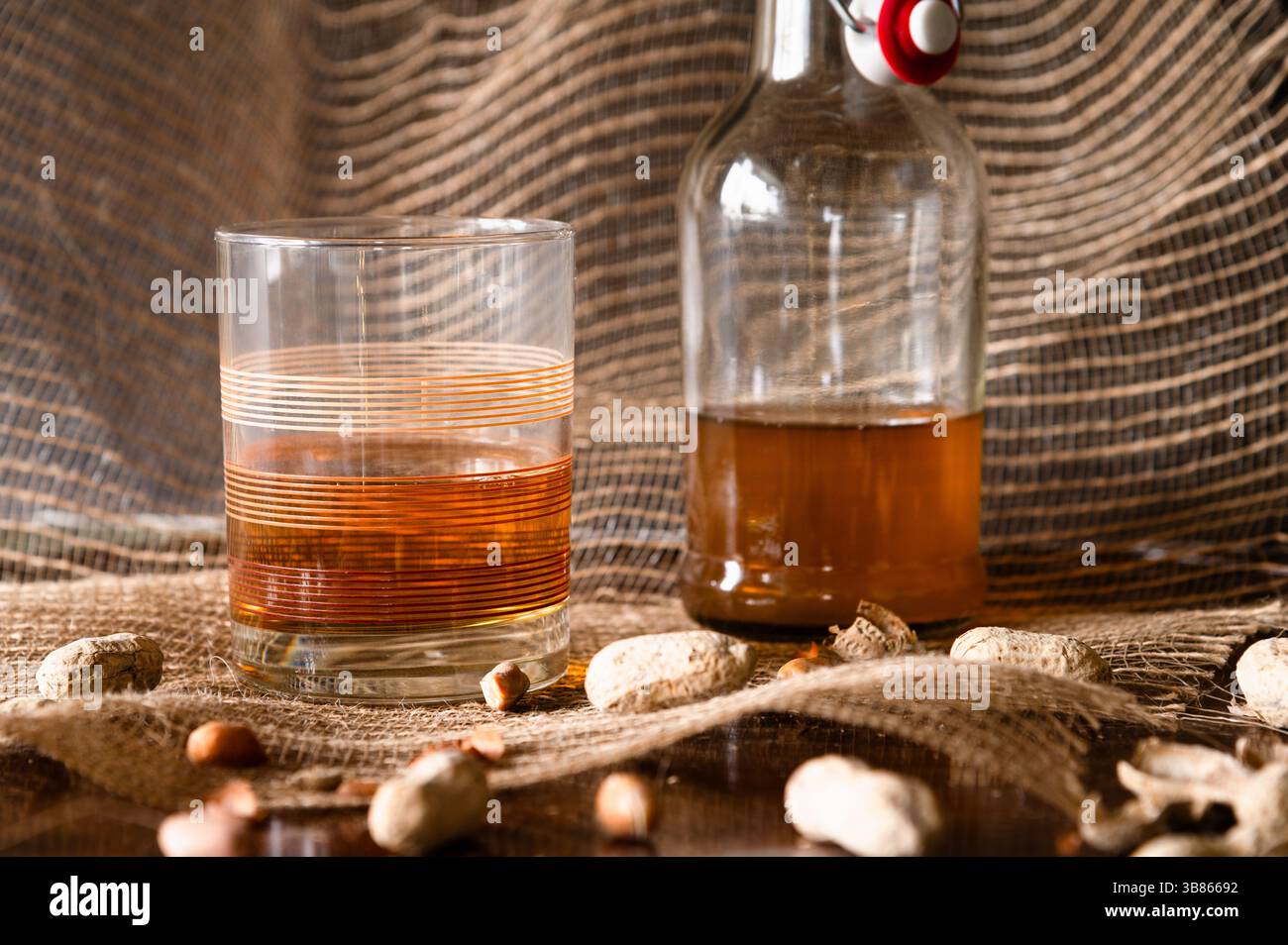 Un bicchiere di pietra vintage e una bottiglia di liquore marrone e arachidi in primo piano Foto Stock