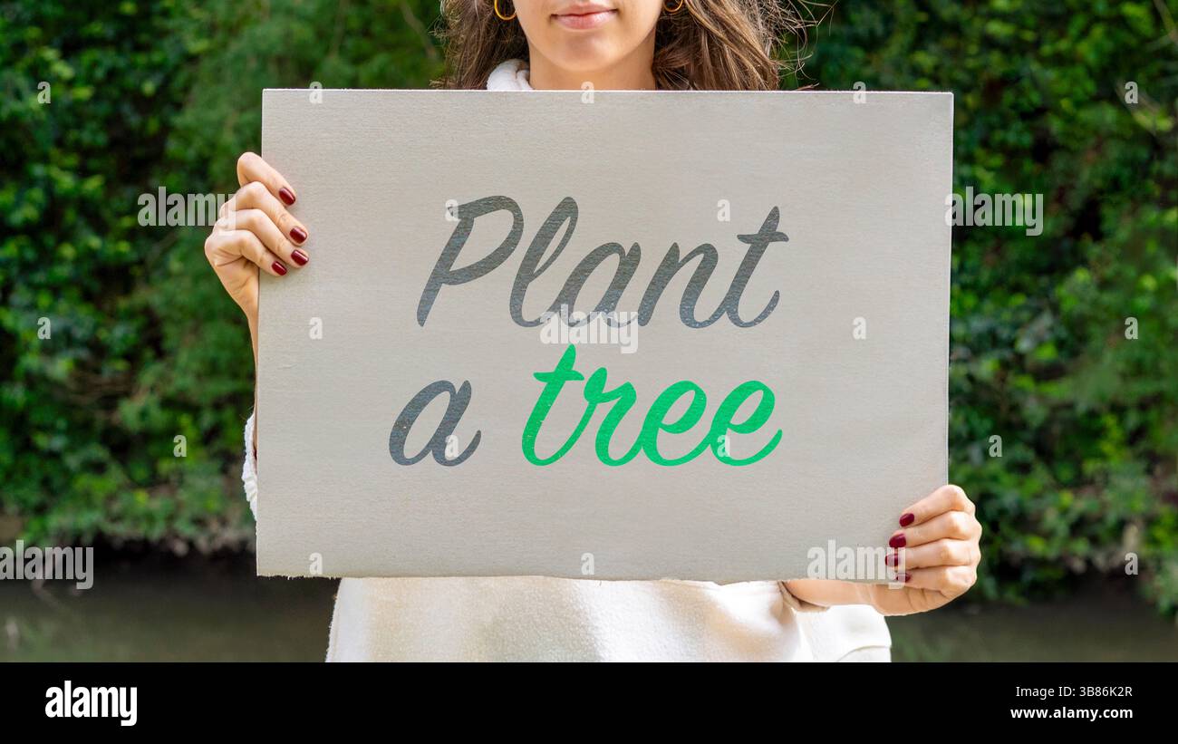Donna che promuove la sostenibilità con un cartello "pianta un albero" vicino al fiume Foto Stock