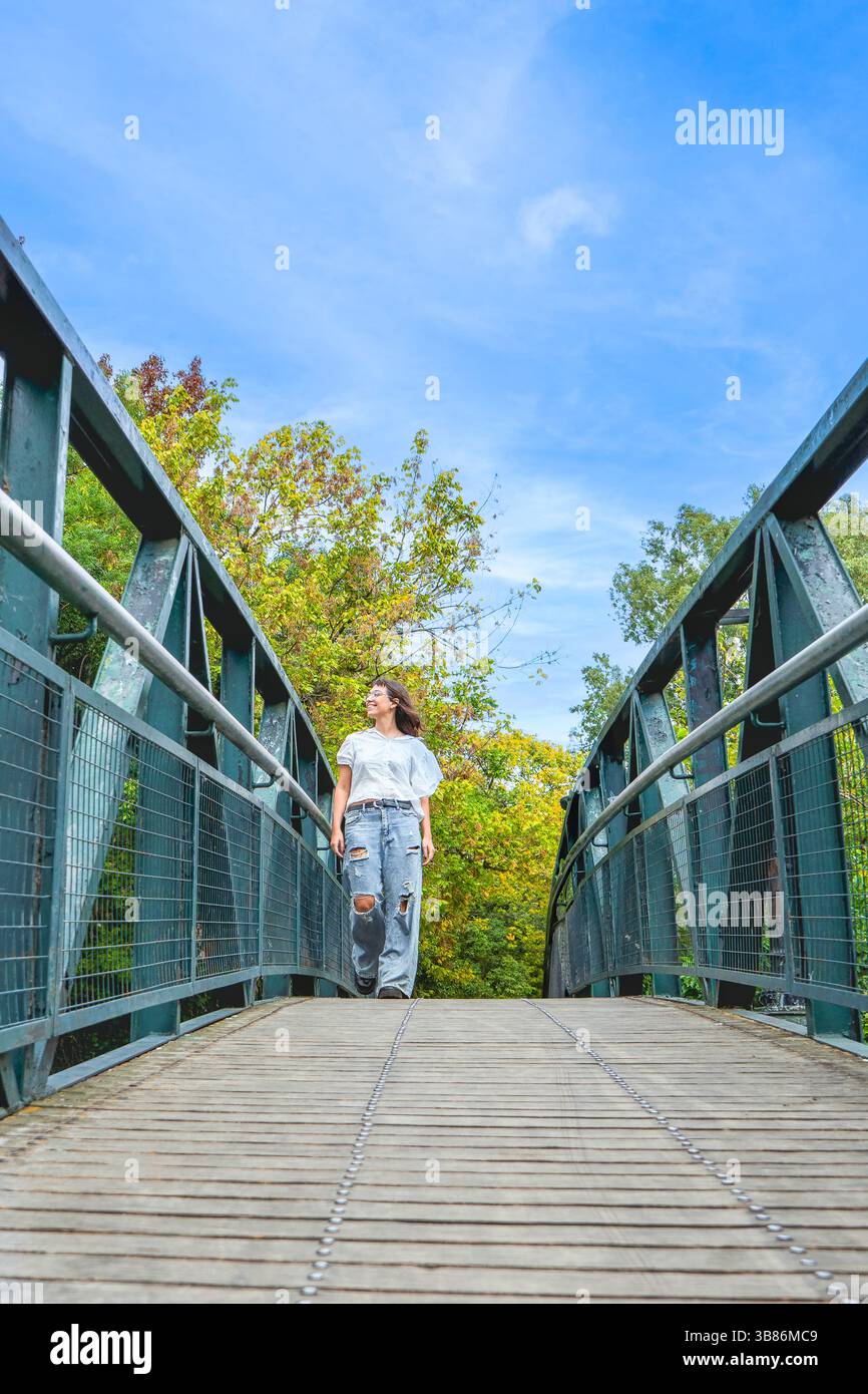 Una giovane donna che cammina attraverso un pittoresco ponte in un parco tranquillo Foto Stock