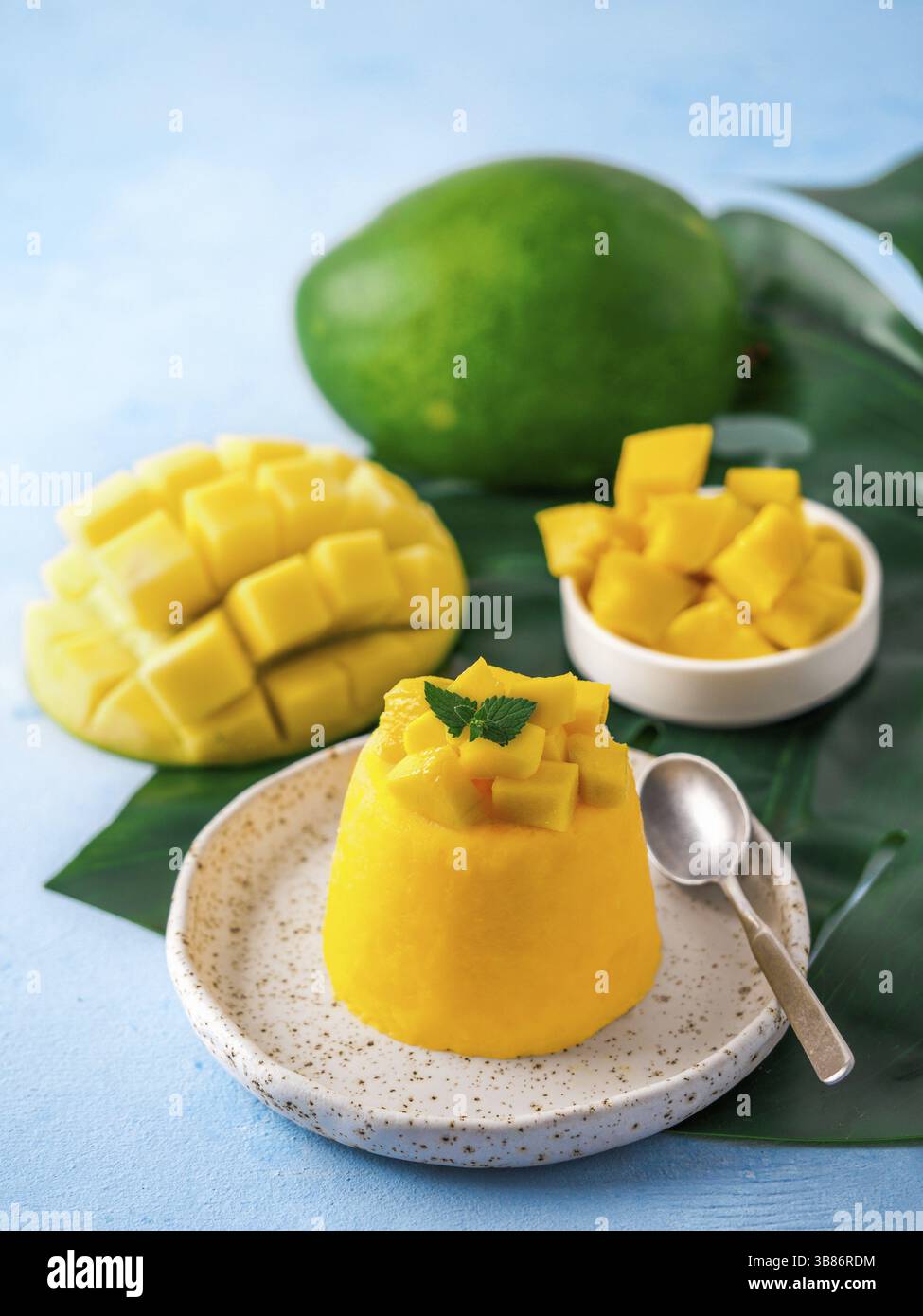 Mousse di mango su sfondo blu con spazio di copia a sinistra. Deliziosa mousse gialla di mango con mango maturo a fette. Verticale Foto Stock