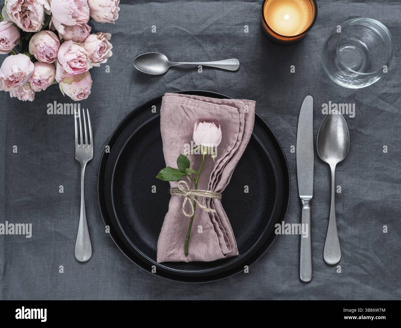 Bella tabella impostazione con candela su grigio tovaglie di lino. Tavola festiva impostazione per nozze cena con spray rosa rosa e rosa tovagliolo sulla piastra. Foto Stock