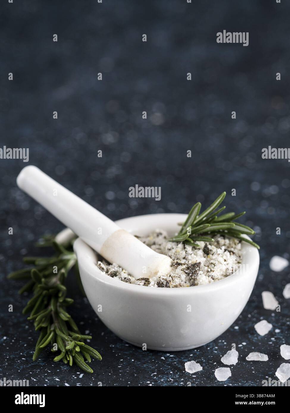Primo piano vista su mortaio e pestello con rosmarino profumato sale marino e scorza di limone. Rosmarino di erbe profumate al sale marino su sfondo blu scuro. Sale profumato Foto Stock