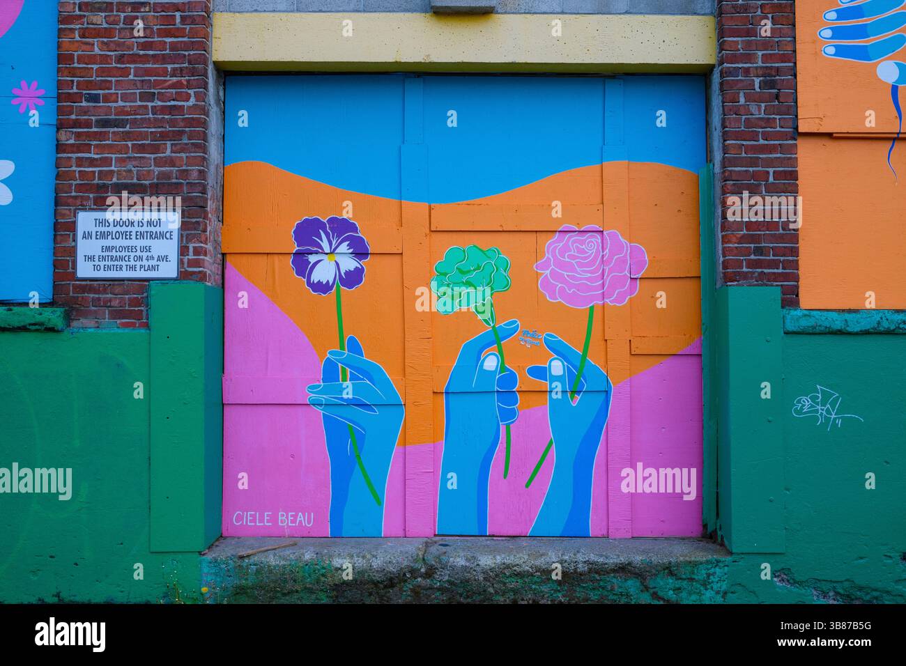 Un colorato murale si trova accanto a una porta a baia su un vecchio edificio in mattoni a Mount Pleasant, Vancouver, BC. Foto Stock
