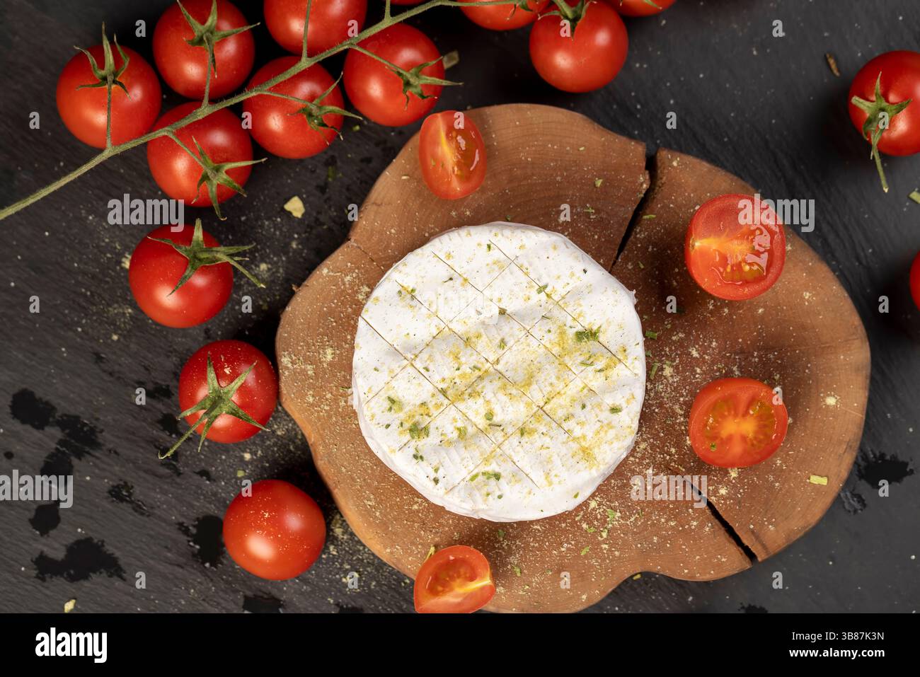 un formaggio morbido con muffa cosparsa di spezie e pomodori, formaggio morbido bianco in sale e spezie e piccoli pomodori rotondi rossi sul tavolo Foto Stock