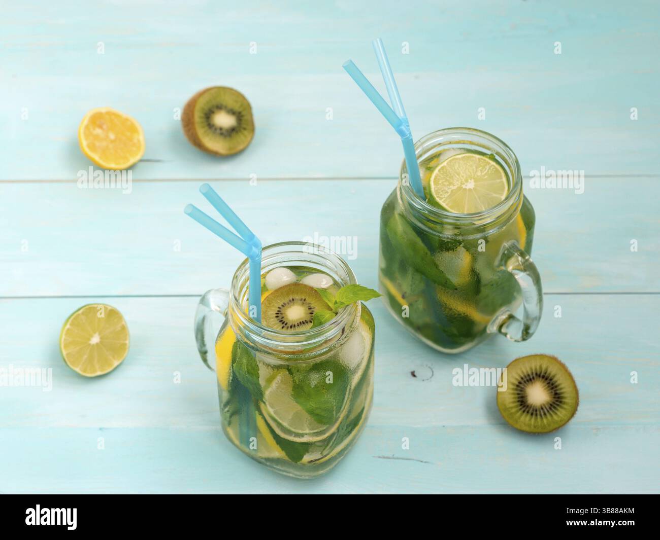 Freddo limonata fatta in casa con limone fresco, calce, kiwi e menta in mason jar. Bevanda estiva sul morbido blu sullo sfondo di legno Foto Stock