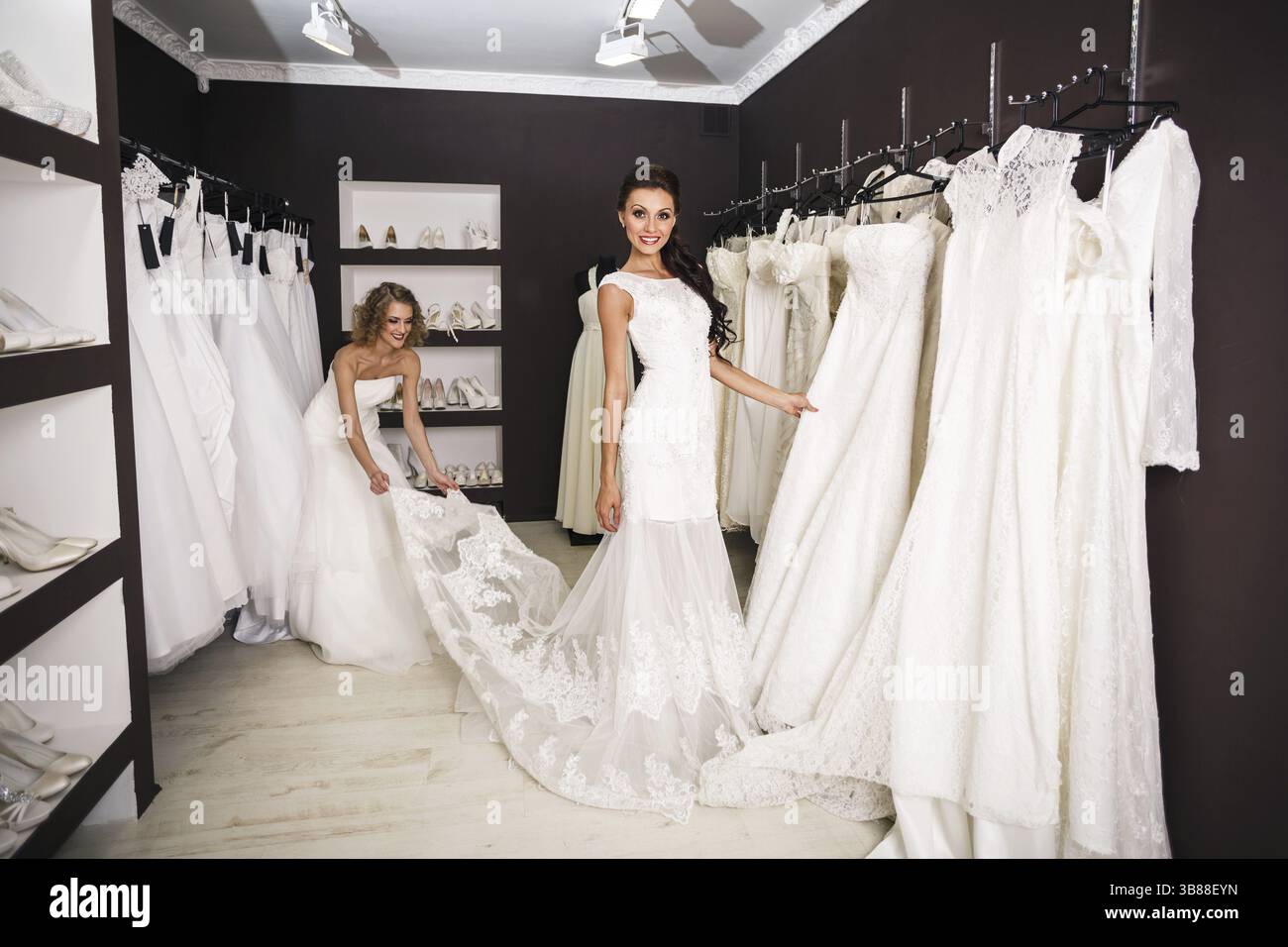 La bella sposa sorridente sceglie un abito bianco nel negozio di moda per matrimoni Foto Stock