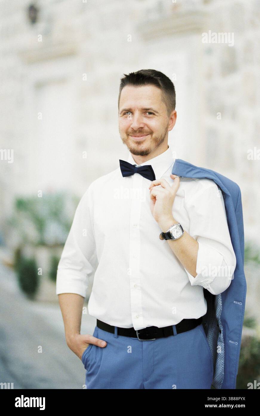 Uomo sorridente che tiene la giacca con la mano sulla spalla mentre è in piedi vicino all'edificio. Foto Stock