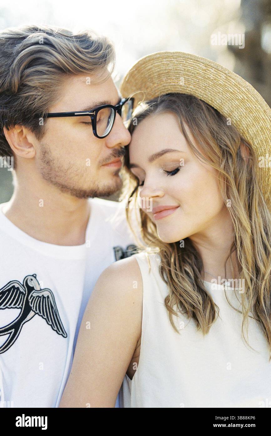 L'uomo con gli occhiali tocca la fronte di una donna con un cappello di paglia. Verticale. Foto Stock
