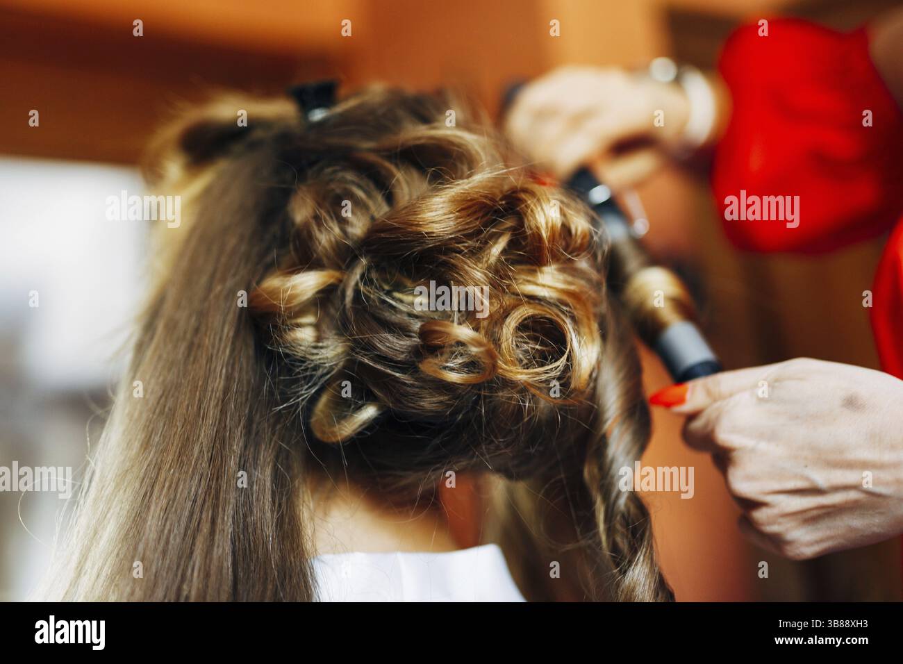 Il parrucchiere rende la sposa uno stile elegante con ricci e un ferro arricciacapelli. Primo piano. Foto Stock
