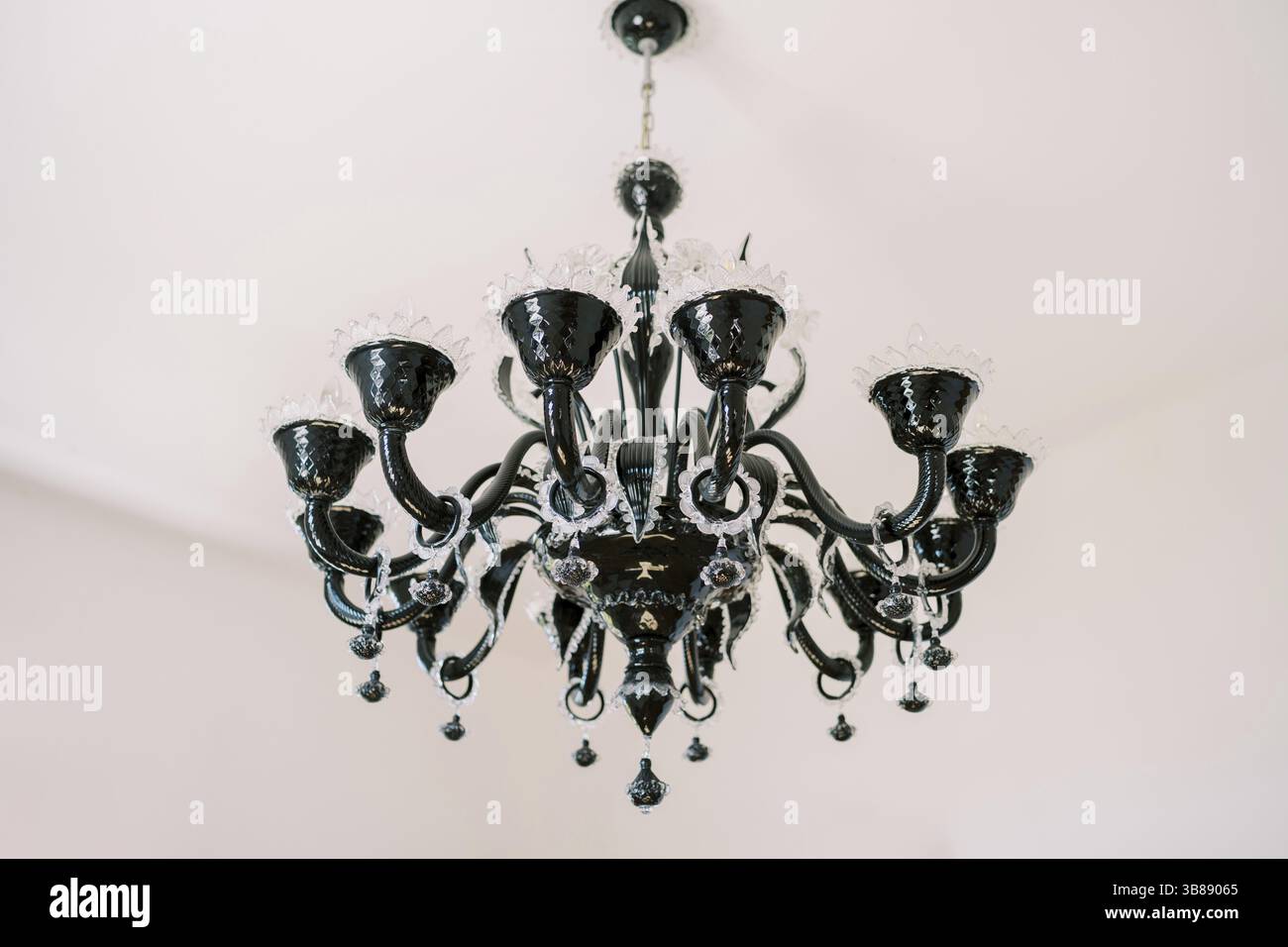 Lampadario nero con decorazioni aperte e pendenti appesi al soffitto bianco della villa. Foto Stock