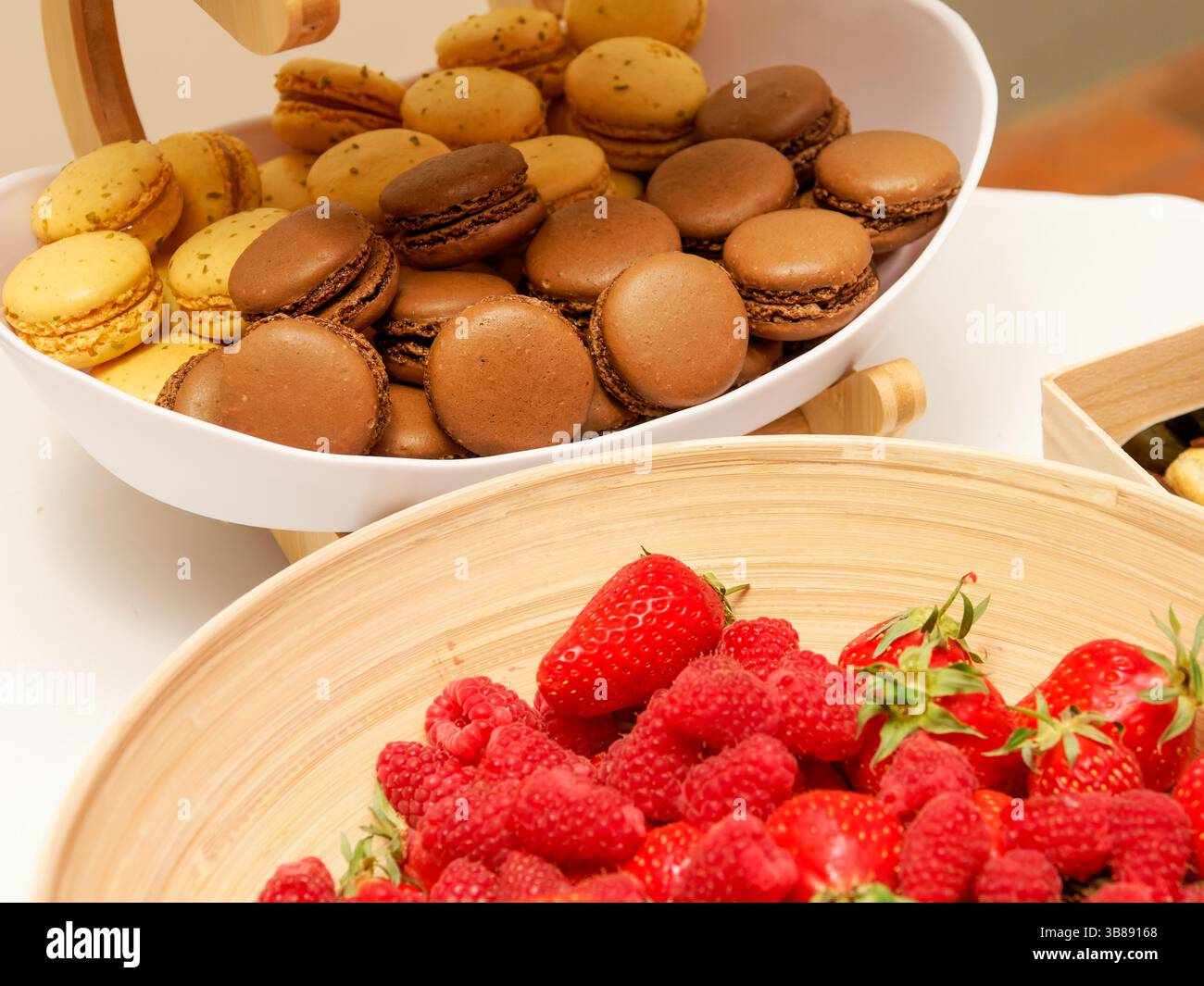 Un assortimento di macaron colorati in una ciotola, accompagnati da fragole e lamponi freschi, perfetti per una vivace esibizione di dessert in una celebrazione Foto Stock